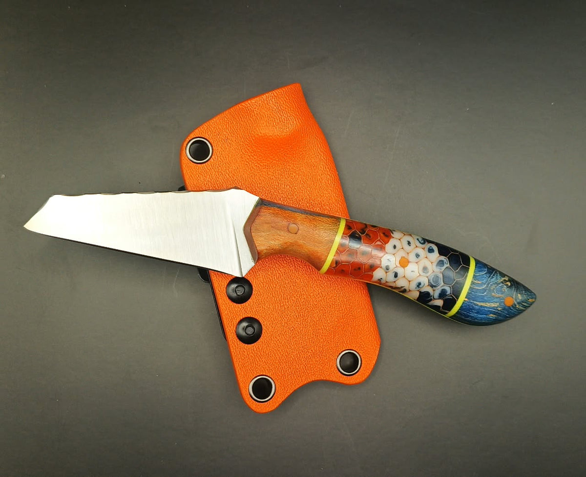 Fixed-blade knife with a multicoloured hybrid handle and orange pins, pictured beside an orange sheath.