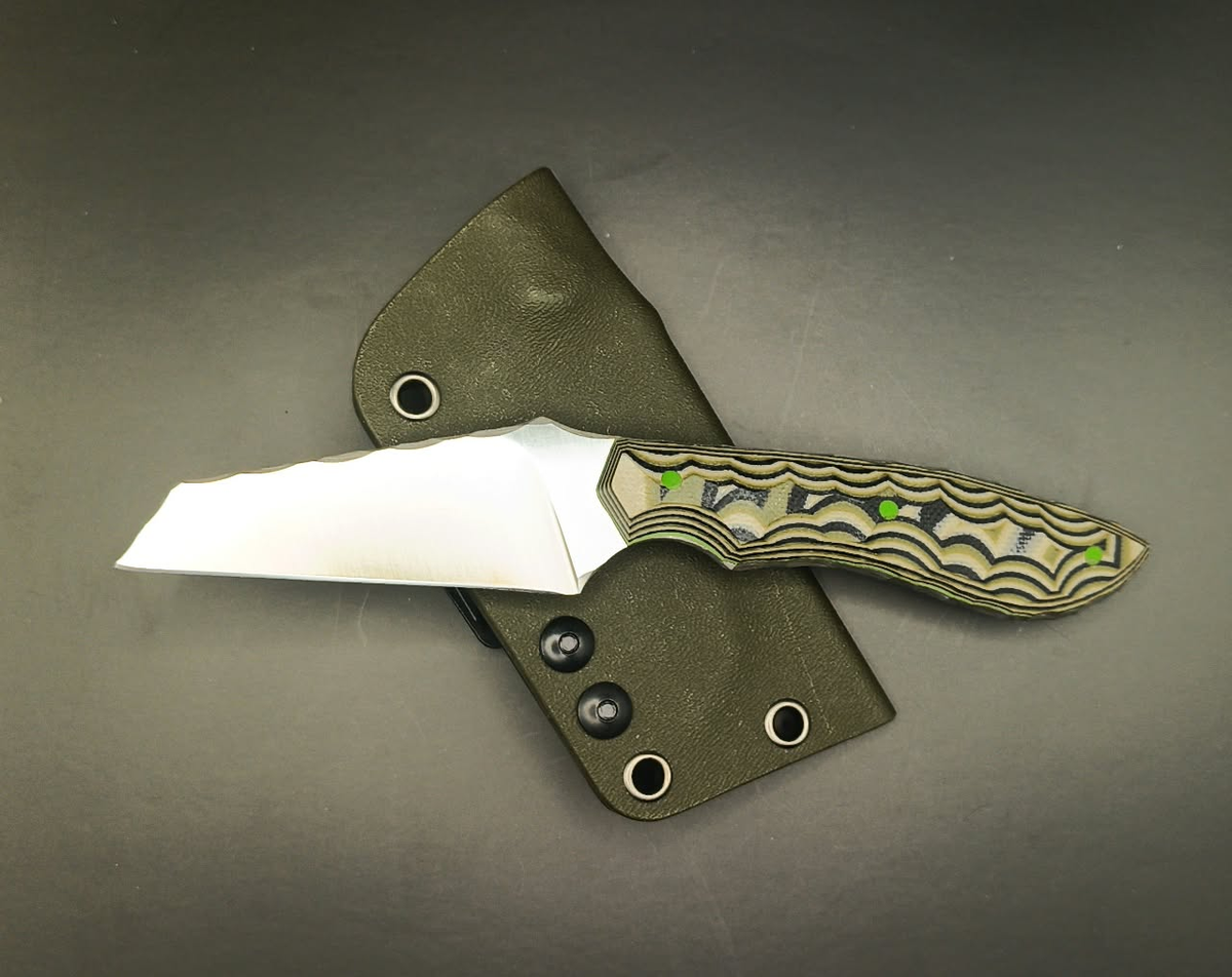 Fixed-blade knife with a layered camo handle and three bright green pins, pictured beside an olive-green sheath.