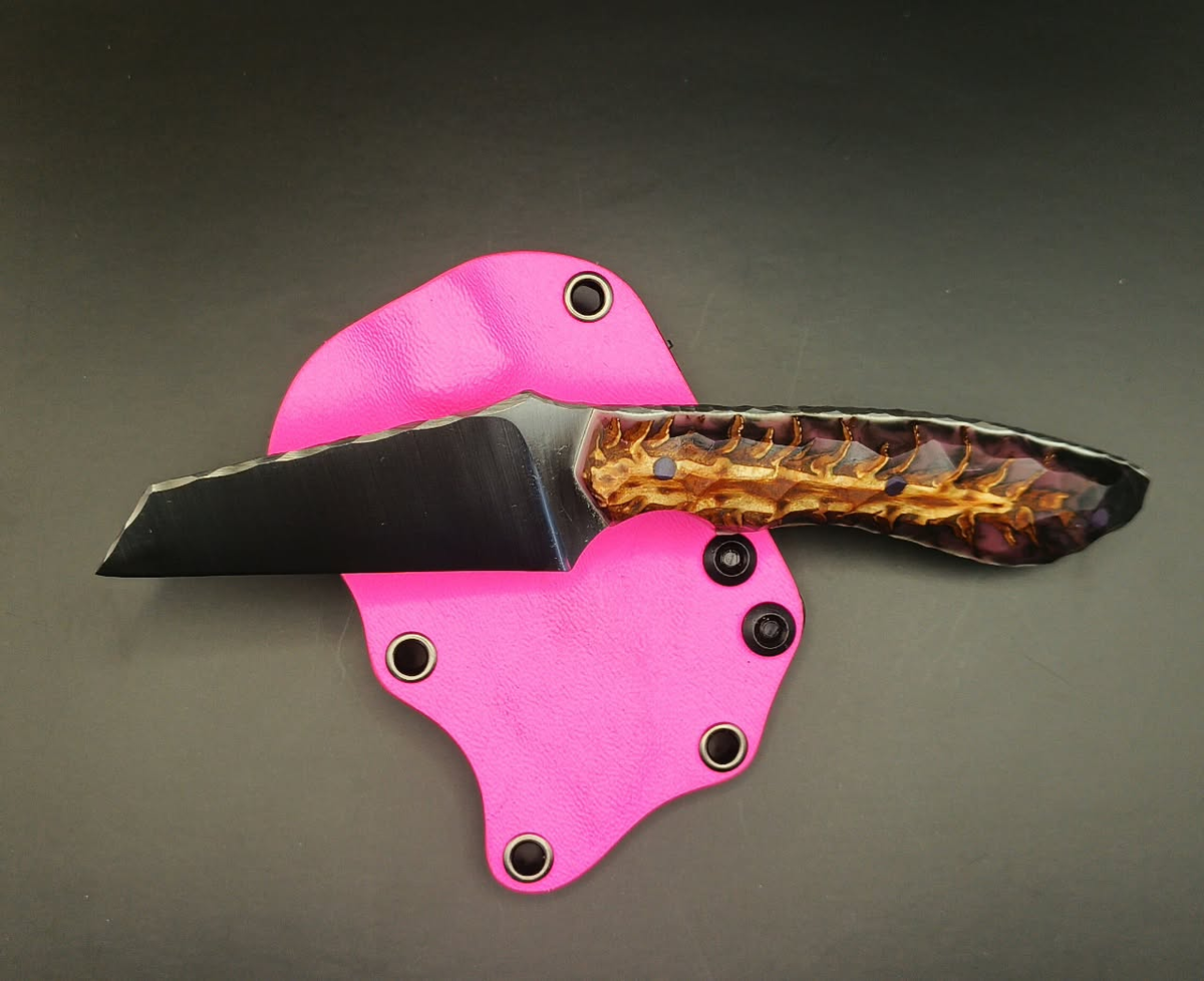 Fixed-blade knife with a patterned pinecone handle and purple pins, pictured beside a bright pink sheath.